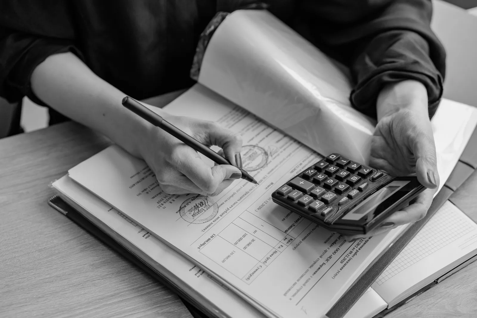 Person using a calculator while signing paperwork at a desk