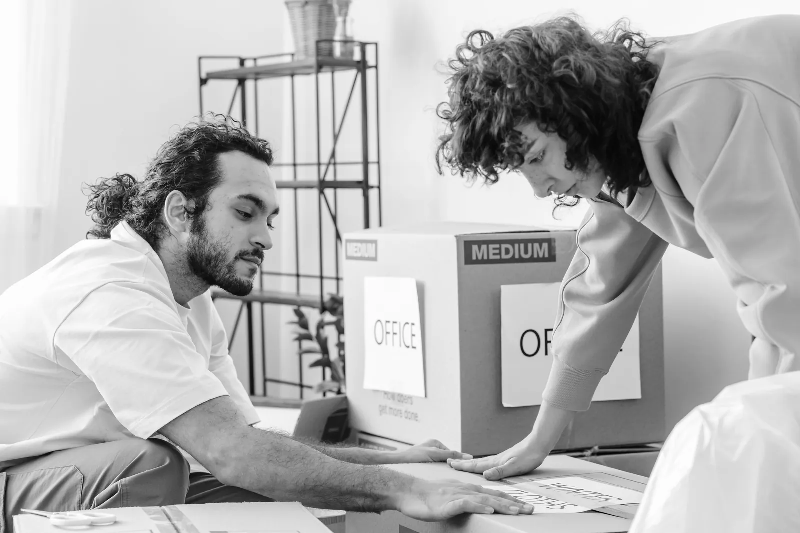 Two people labeling cardboard boxes packed with office supplies