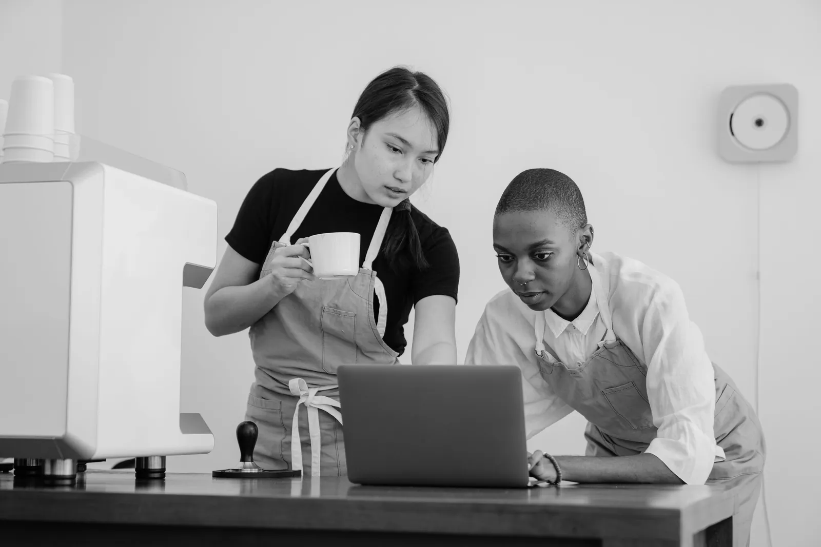 Two coworkers standing at a table while one shows the other a program on a laptop