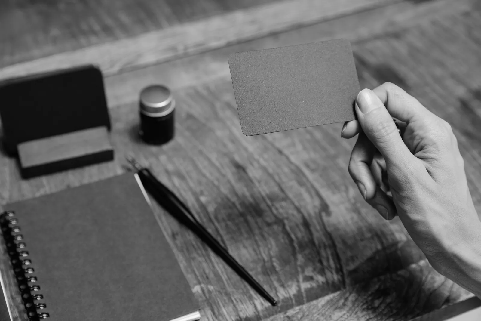 Hand holding a blank black business card above a wooden desk