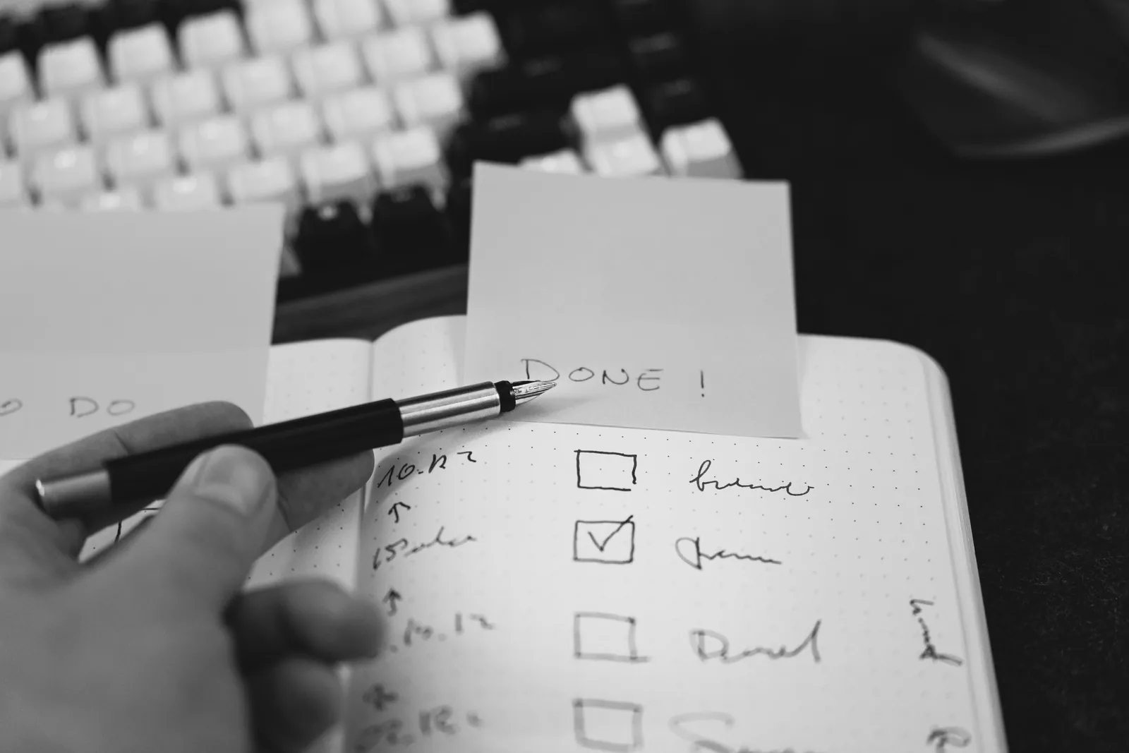Hand holding a pen over a notebook checklist with a sticky note