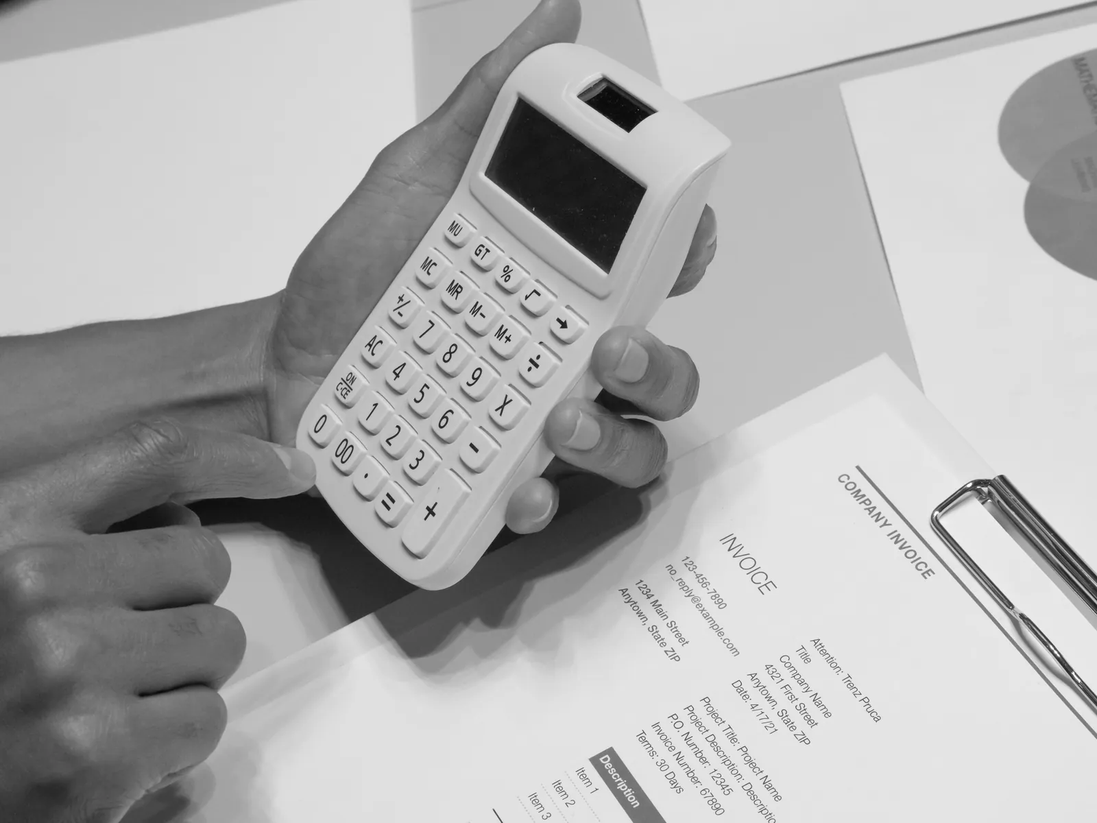 Hands using a calculator beside a printed company invoice