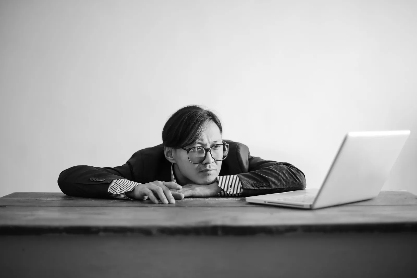 Man in glasses resting his head on a tablet while looking at a laptop