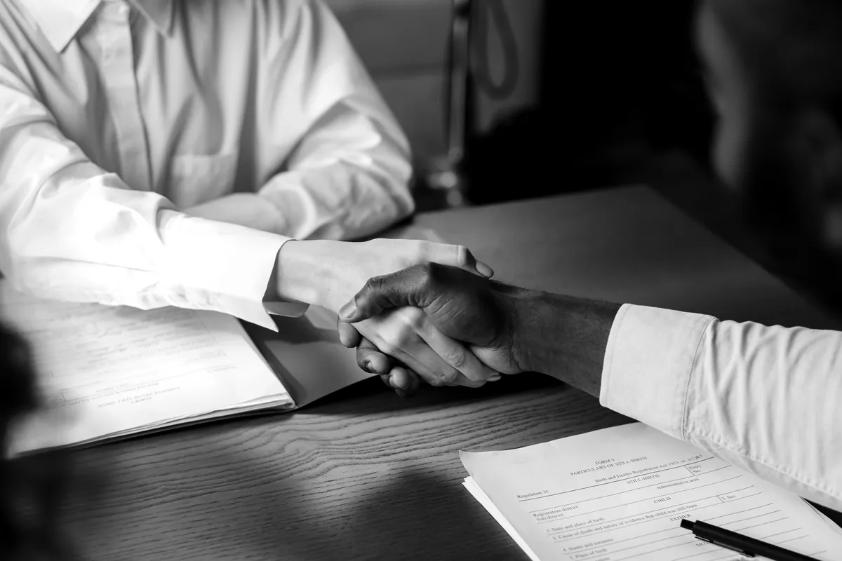 Two people shaking hands across a desk over a signed contract