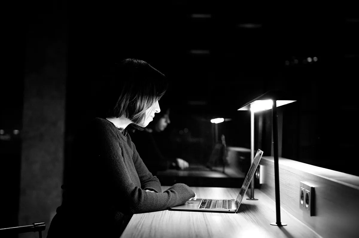 Woman working late on a laptop at a desk lamp